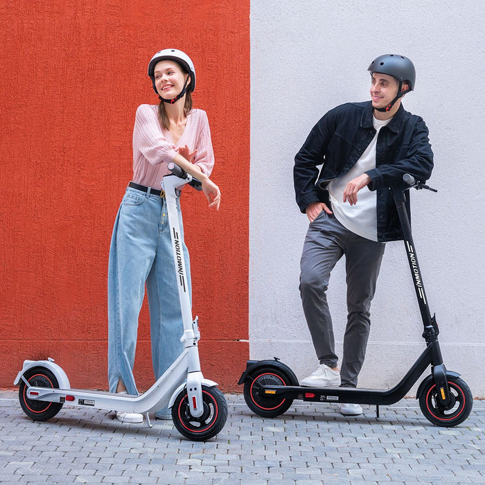 Two people standing with electric scooters against a red and gray wall.
