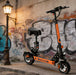 Orange electric scooter parked on a street with graffiti in the background
