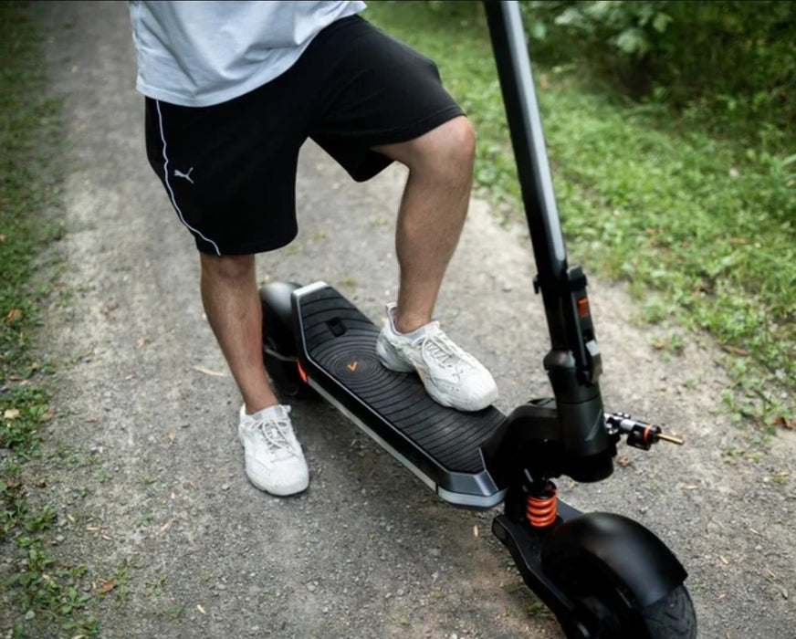 Person riding in Apollo Phantom 2 scooter on a paved path with grass on either side.