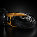 Close-up of a rugged off-road vehicle or RC crawler rear wheel assembly, featuring a black knobby tire, silver disc brake, and prominent gold suspension components against a dark studio background.